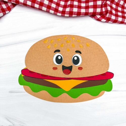 A completed hamburger paper craft with a smiling cartoon face, colorful burger layers, and sesame seeds on the bun.