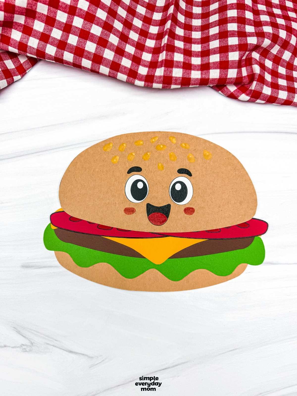 A completed hamburger paper craft with a smiling cartoon face, colorful burger layers, and sesame seeds on the bun.