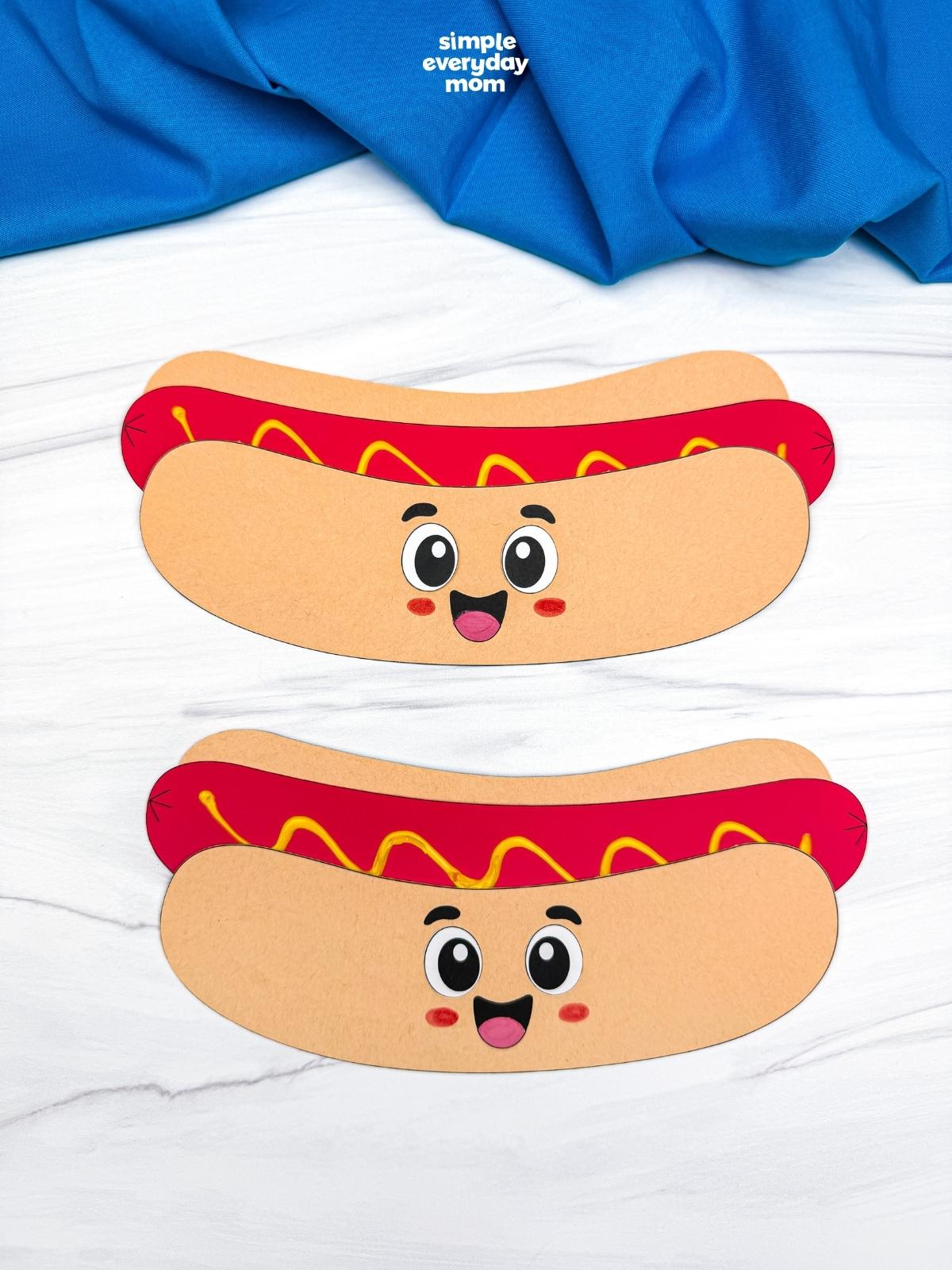 A completed Craft showing two smiling paper hot dog crafts with mustard topping on a white tabletop.