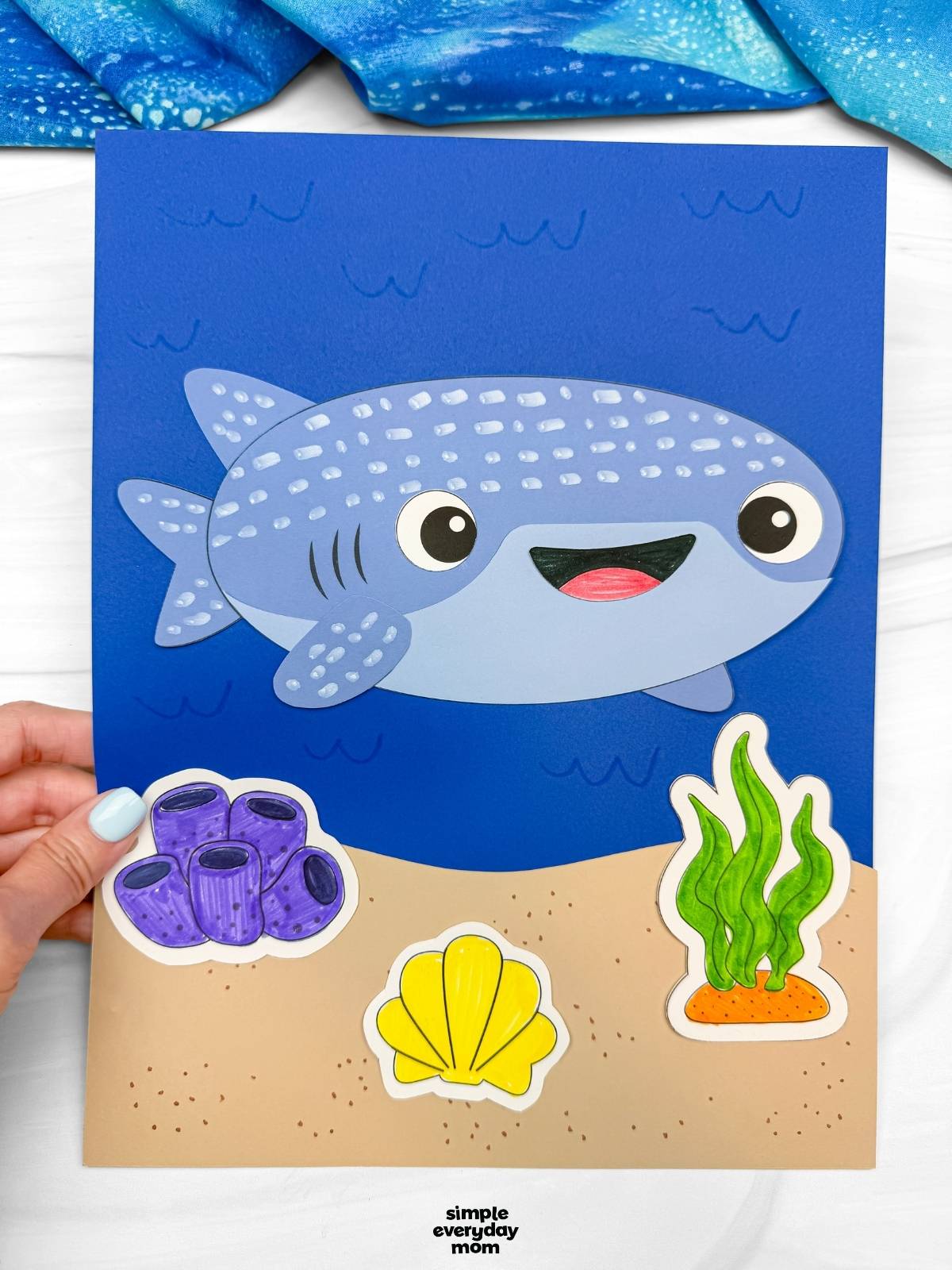 A completed Craft showing a whale shark paper craft on a blue ocean background with seaweed, coral, and shell decorations.