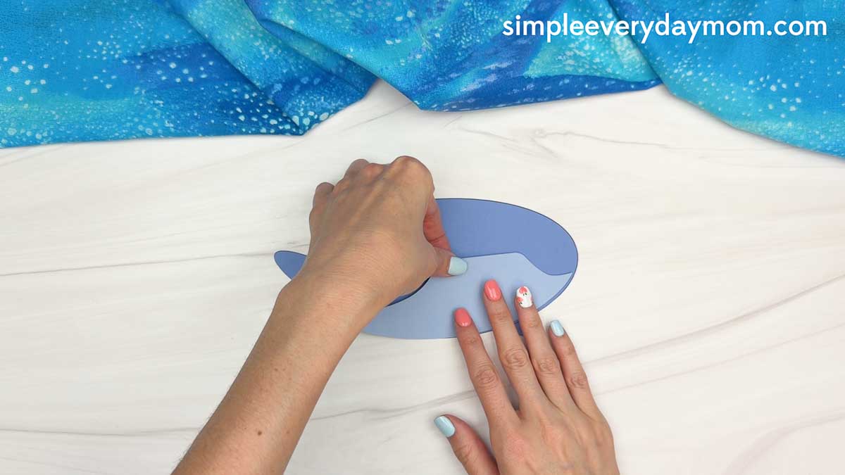 Hands assembling the whale shark paper craft by pressing the body pieces together on a white tabletop.