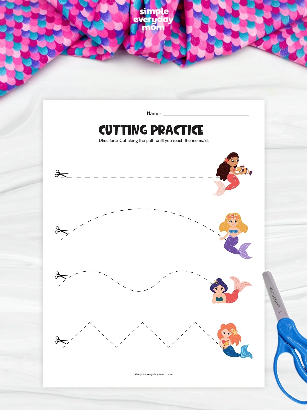 This image features a mermaid-themed cutting practice worksheet designed to help young children develop scissor skills. The page includes four different dashed-line paths—straight, curved, wavy, and zigzag—that children can cut along to reach the mermaids at the end of each line. A pair of blue safety scissors is placed beside the worksheet, reinforcing the hands-on cutting activity.