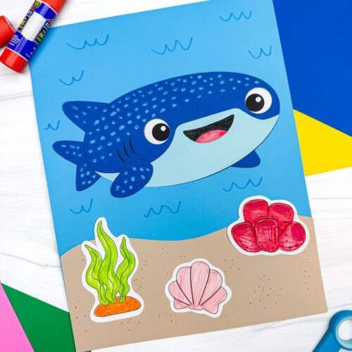 A completed Craft showing a whale shark paper craft on an ocean scene with seaweed, coral, and shell decorations surrounded by craft supplies.