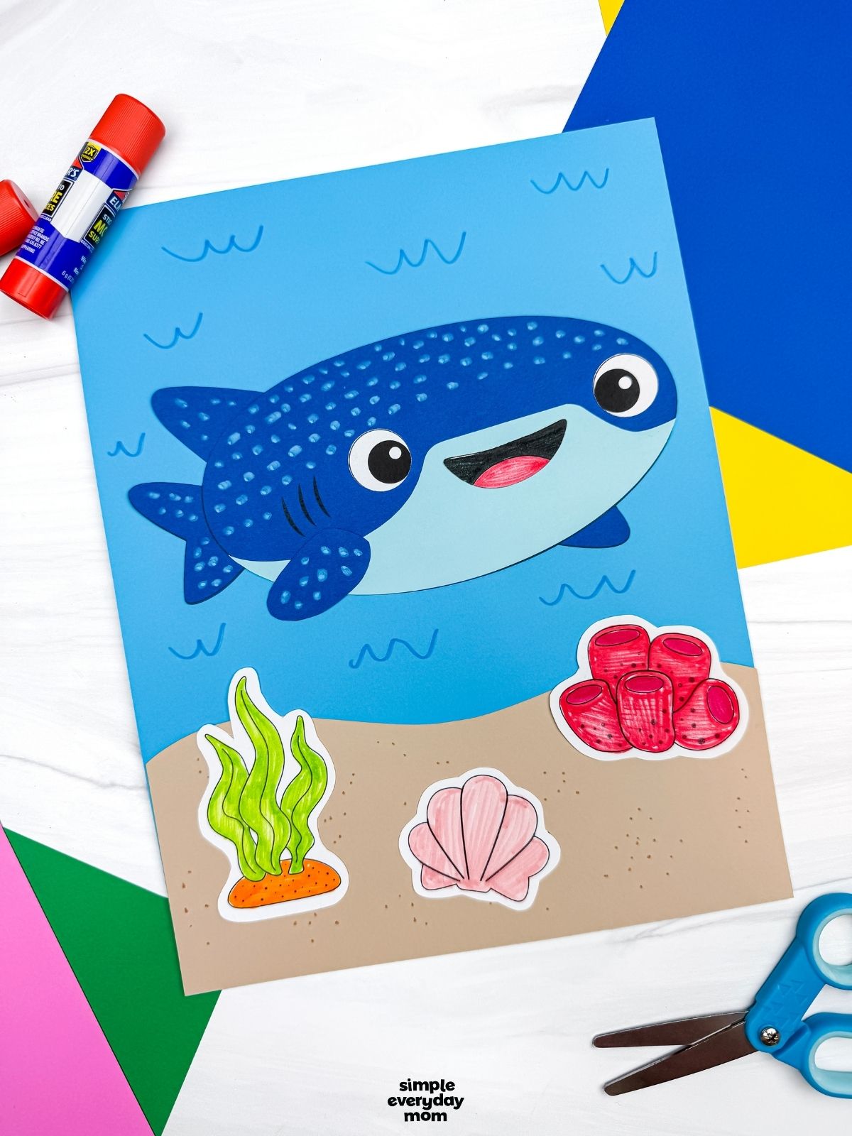 A completed Craft showing a whale shark paper craft on an ocean scene with seaweed, coral, and shell decorations surrounded by craft supplies.