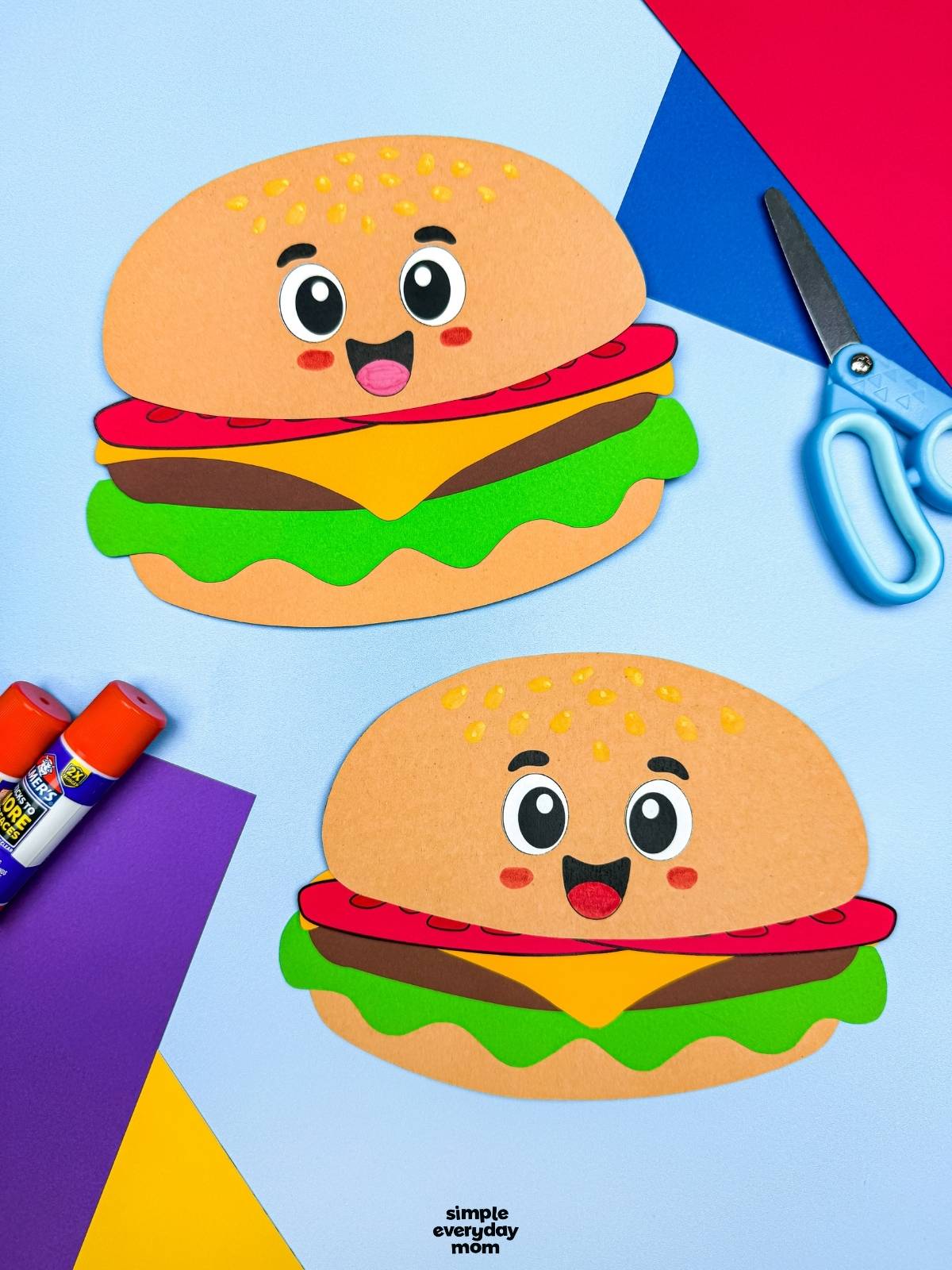 A completed hamburger paper craft displayed with colorful cardstock, glue sticks, and scissors on a craft workspace.