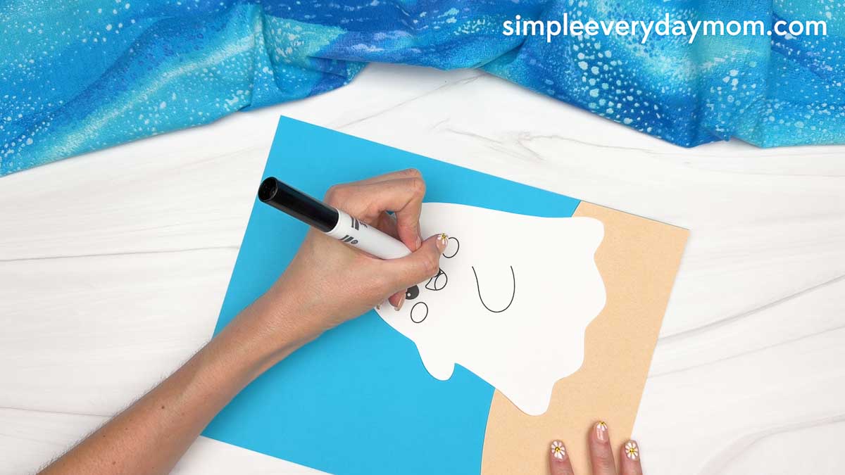 Hands drawing facial details on a ghost cutout for a beach ghost craft scene.