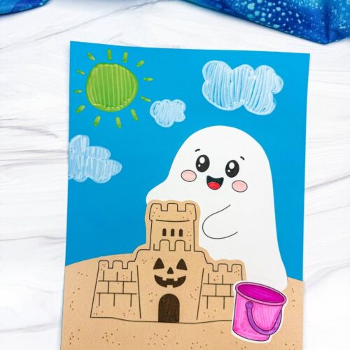 A completed Craft featuring a smiling beach ghost behind a sandcastle with a pink beach bucket, sunny sky, and fluffy clo