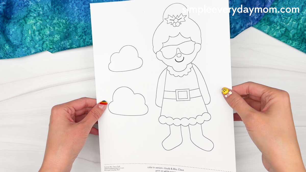 Hands holding the Summer Mrs. Claus printable template with cloud cutouts.