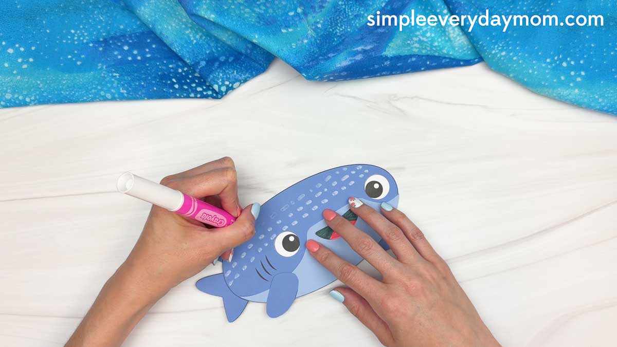 Hands drawing white spots on the whale shark paper craft with a marker to create the whale shark's distinctive pattern.