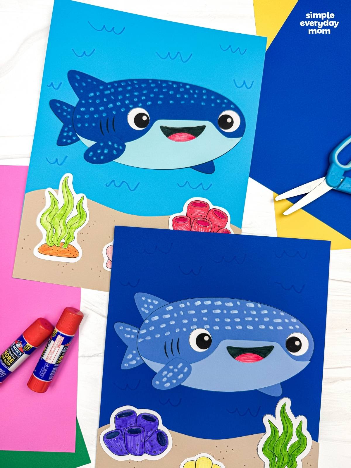 A completed Craft showing two whale shark paper crafts on ocean themed backgrounds with seaweed, coral, and colorful craft supplies nearby.