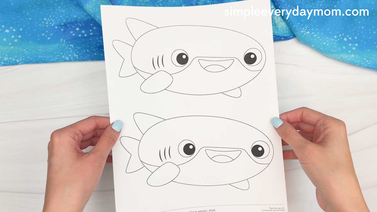 Hands holding a printable whale shark craft template sheet with two black and white whale shark outlines ready for coloring and cutting.