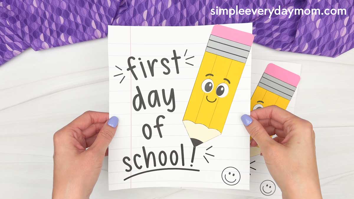 Hands hold a first day of school card with a smiling pencil craft attached to the front.