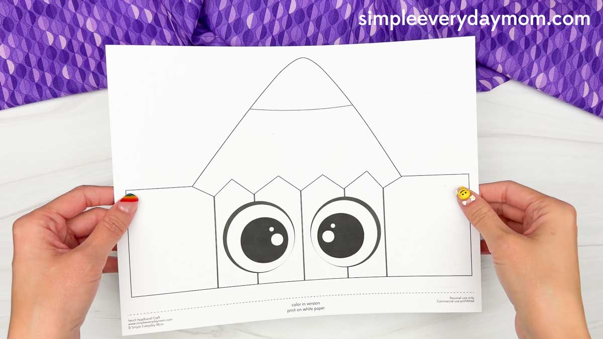 Hands hold the printable pencil craft template with large eyes and foldable side flaps.
