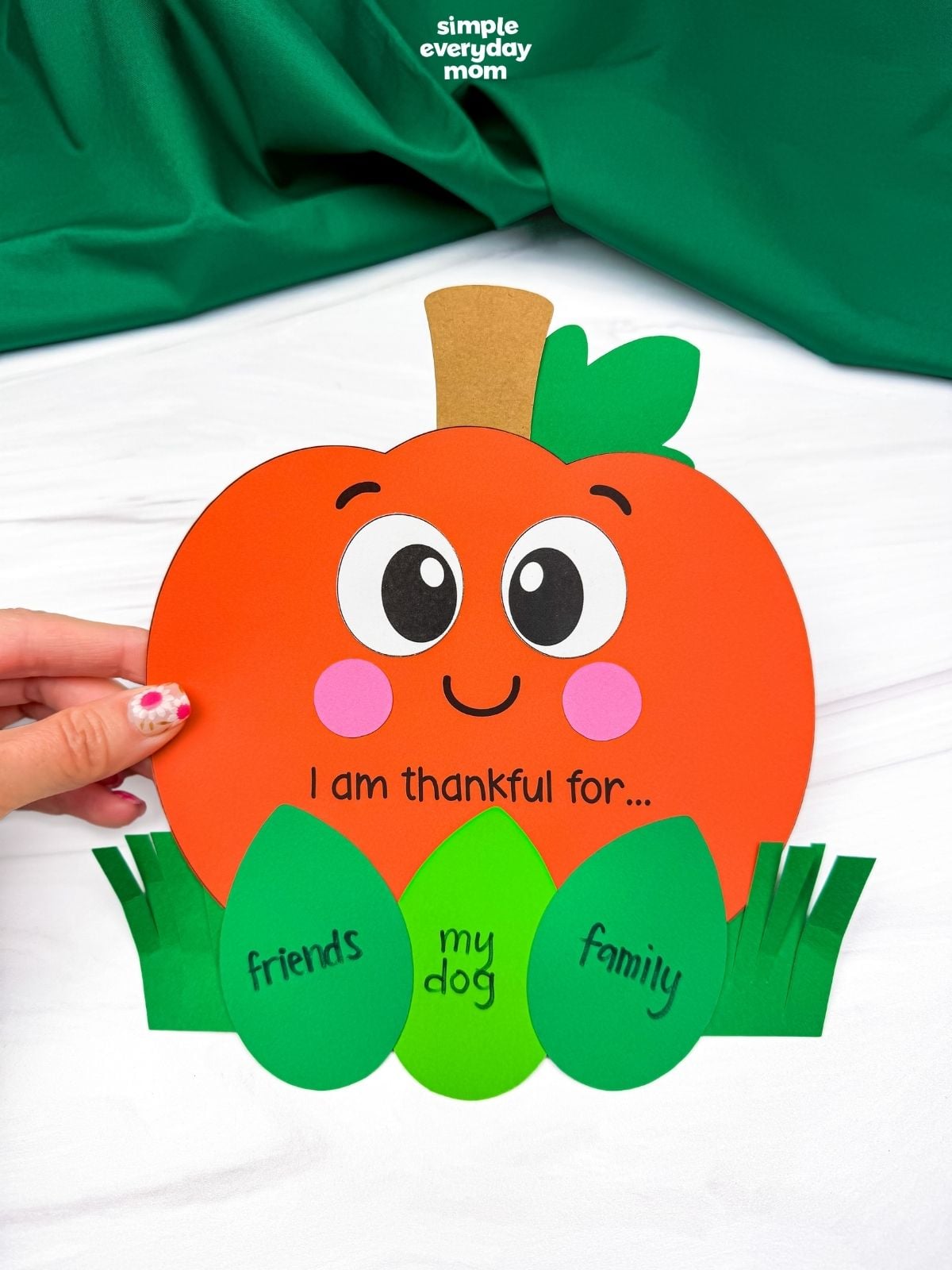 Hands holding the completed thankful pumpkin craft with gratitude leaf inserts tucked into the grass pockets.