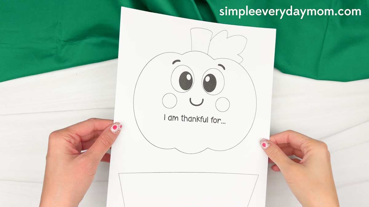 Hands holding the printable thankful pumpkin craft template with a pumpkin outline and writing prompt ready to decorate.