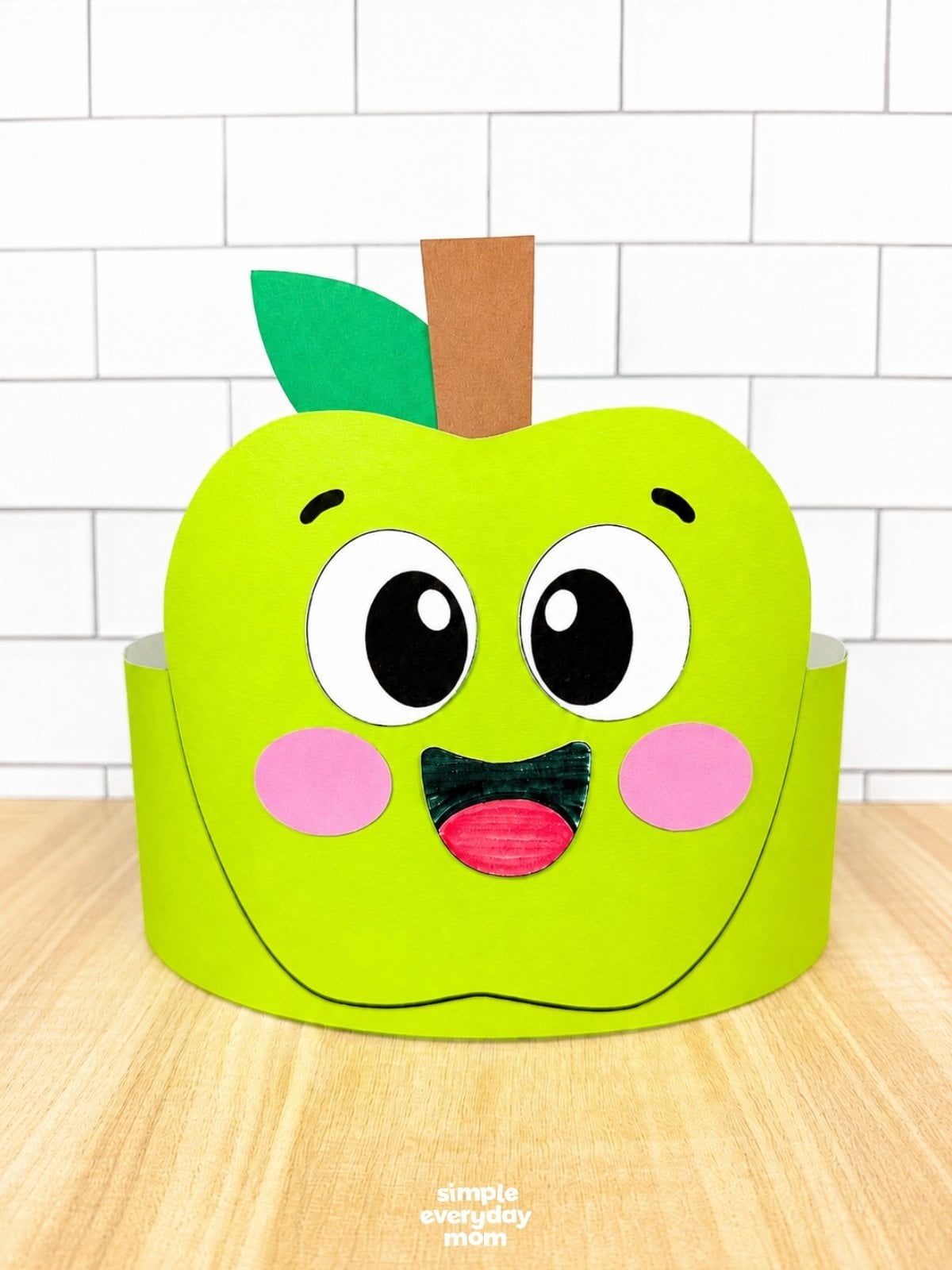 A completed craft of a green apple headband with a smiling face, leaf, and stem ready to wear.