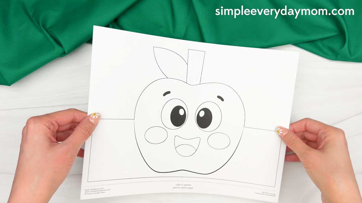 Hands holding the printable apple headband template before cutting out the craft pieces.