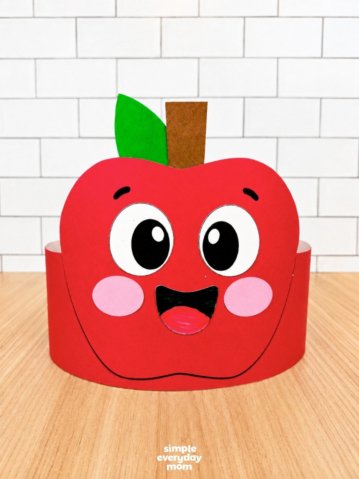 A completed craft of a red apple headband with a smiling face, leaf, and stem ready to wear.