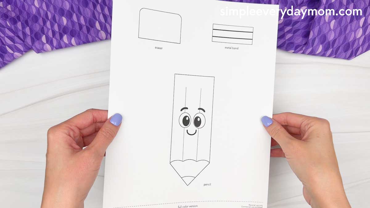 Hands hold the printable template with the pencil, eraser, and metal band pieces for the back to school pencil craft.