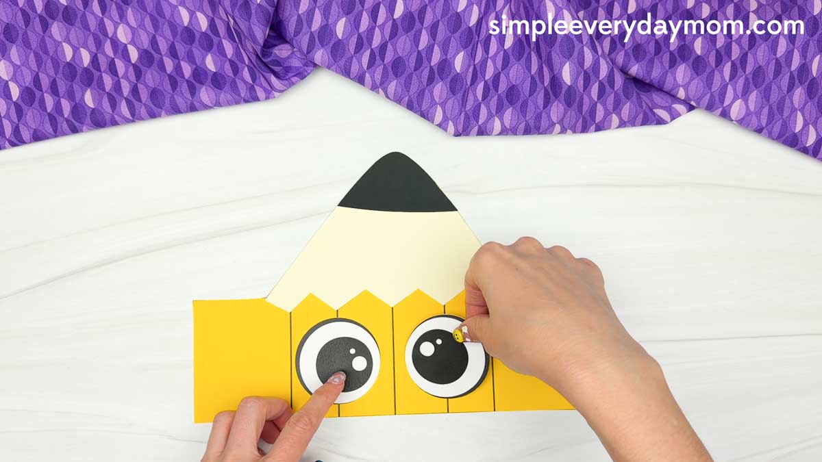 Hands glue the large eye pieces onto the printable pencil craft template.