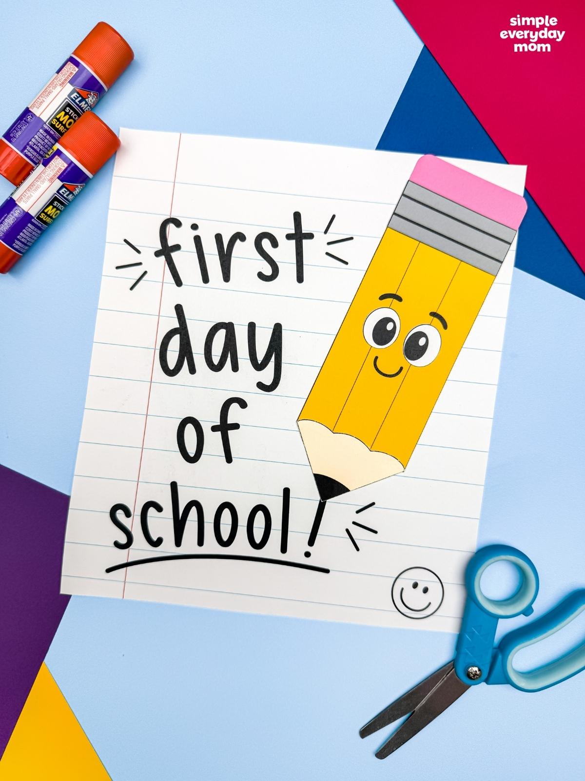 A completed craft featuring a smiling pencil on a first day of school notebook paper with craft supplies nearby.
