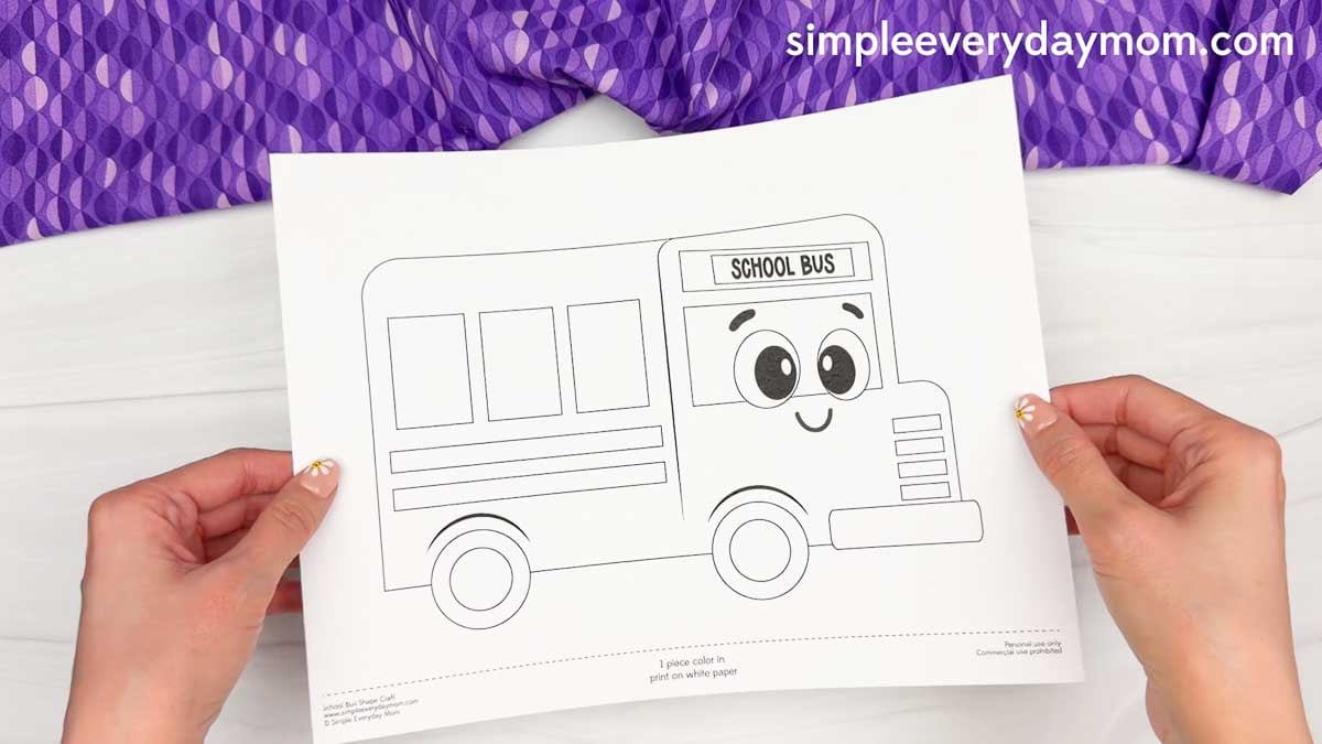 Hands holding the black and white printable bus shape craft template ready to color and assemble.