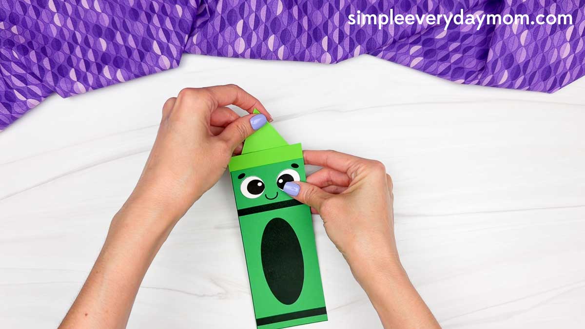 Hands sliding the crayon tip into the top of the crayon shape craft while holding the face in place.