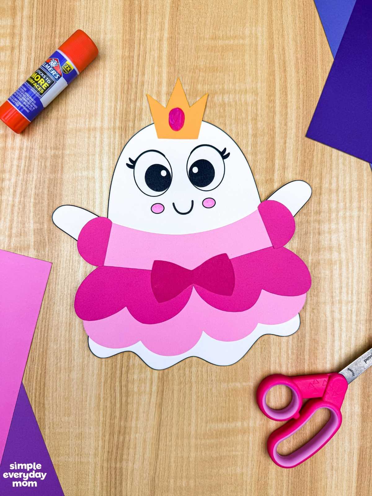 A completed craft of the Princess Ghost Disguise Craft featuring a layered princess dress, bow, sleeves, and crown displayed with craft supplies.
