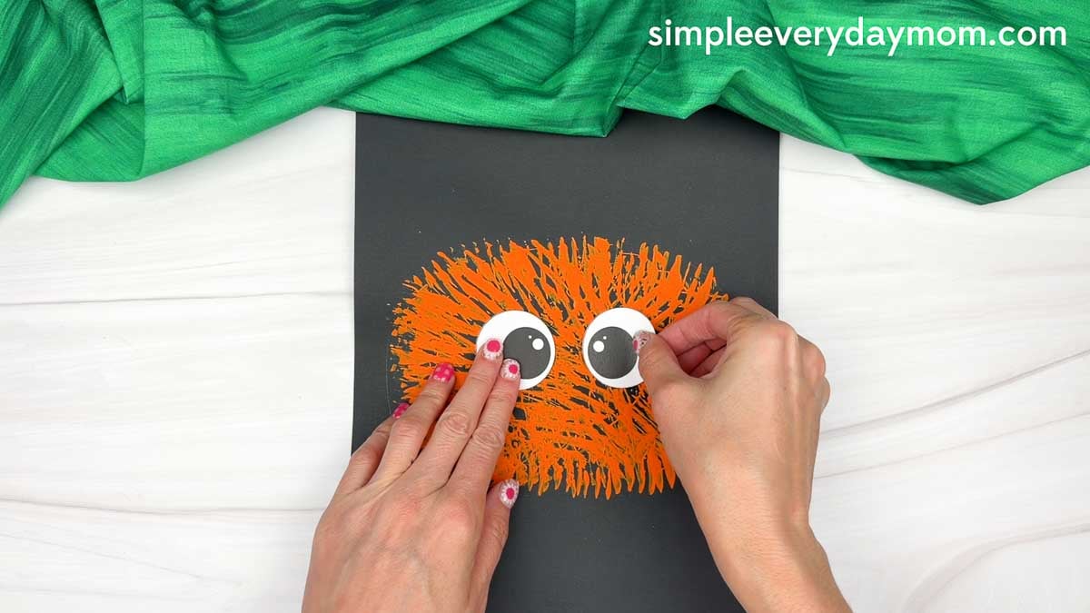 Hands gluing the eye pieces near the top center of the fork painted pumpkin.