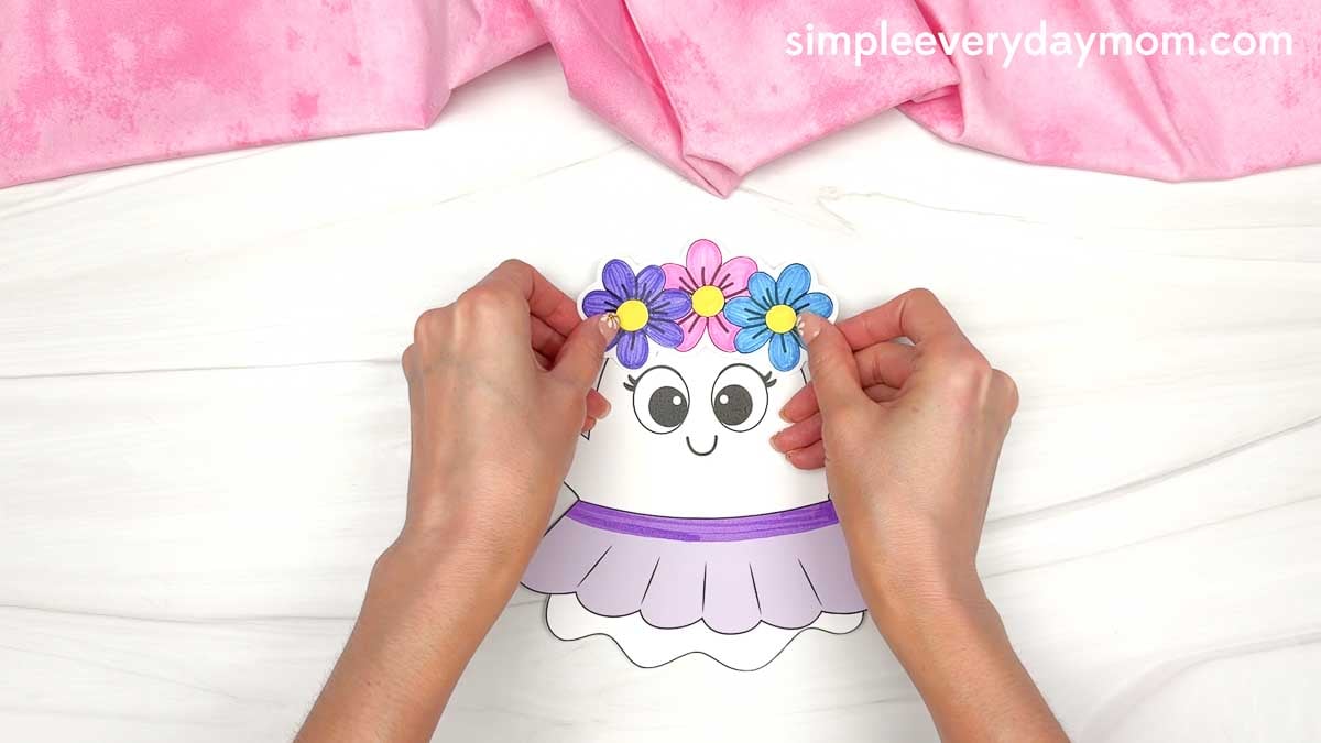 Hands positioning the flower crown onto the Fairy Ghost Disguise Craft head before gluing it in place.