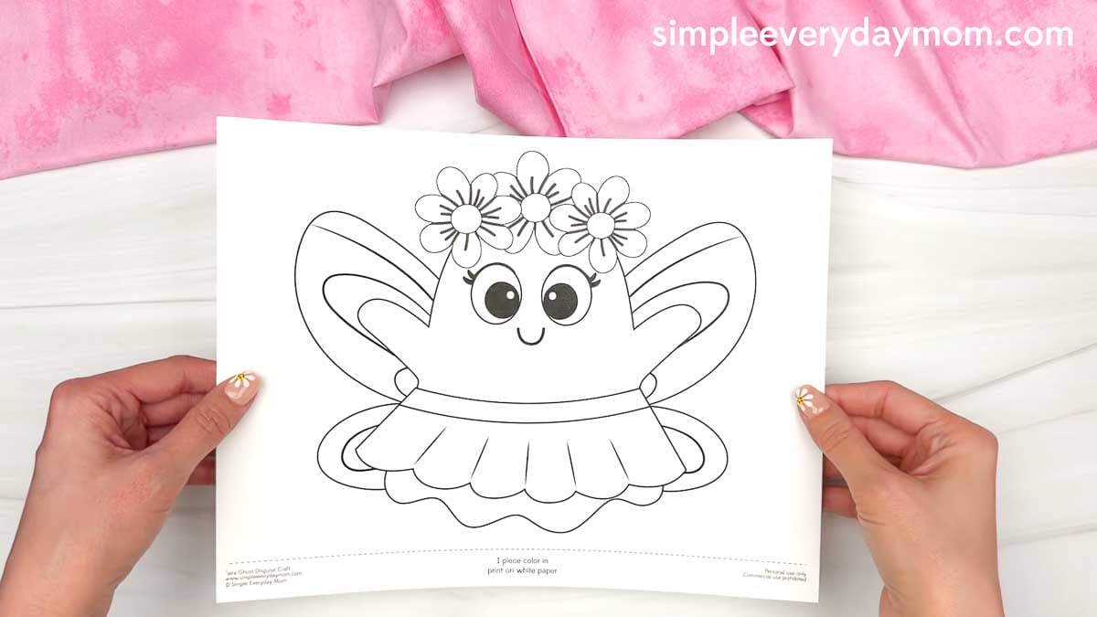 Hands holding the Fairy Ghost Disguise Craft printable template with fairy wings, a flower crown, and a skirt ready to color.