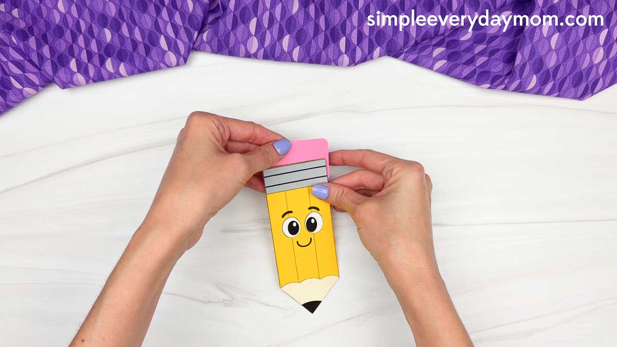 Hands align the pink eraser piece with the top of the smiling pencil craft.