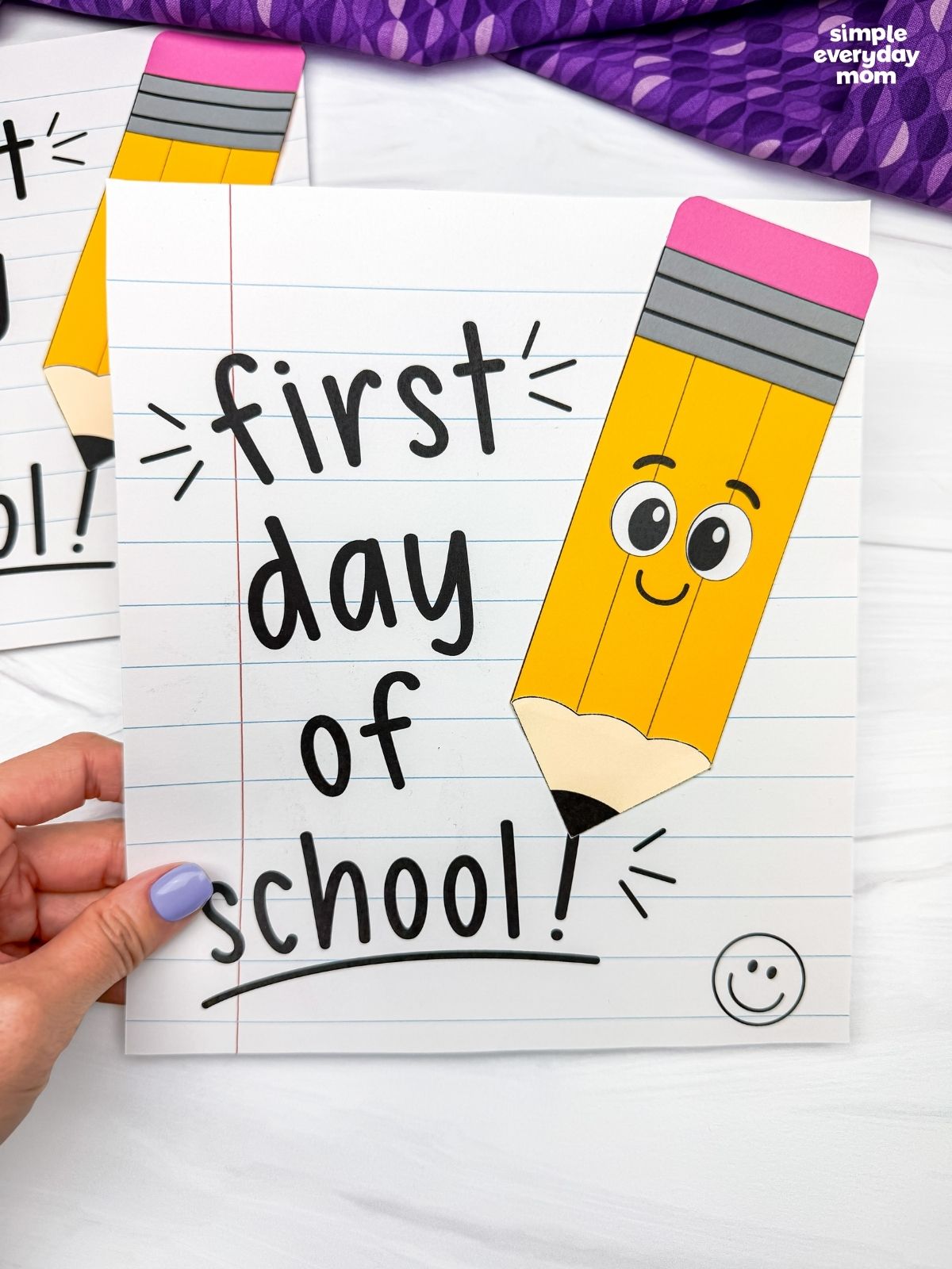 Hands hold the completed back to school pencil craft on a first day of school notebook paper.