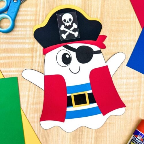 A completed craft of a pirate ghost disguise displayed with colorful paper, scissors, and a glue stick on a craft table.