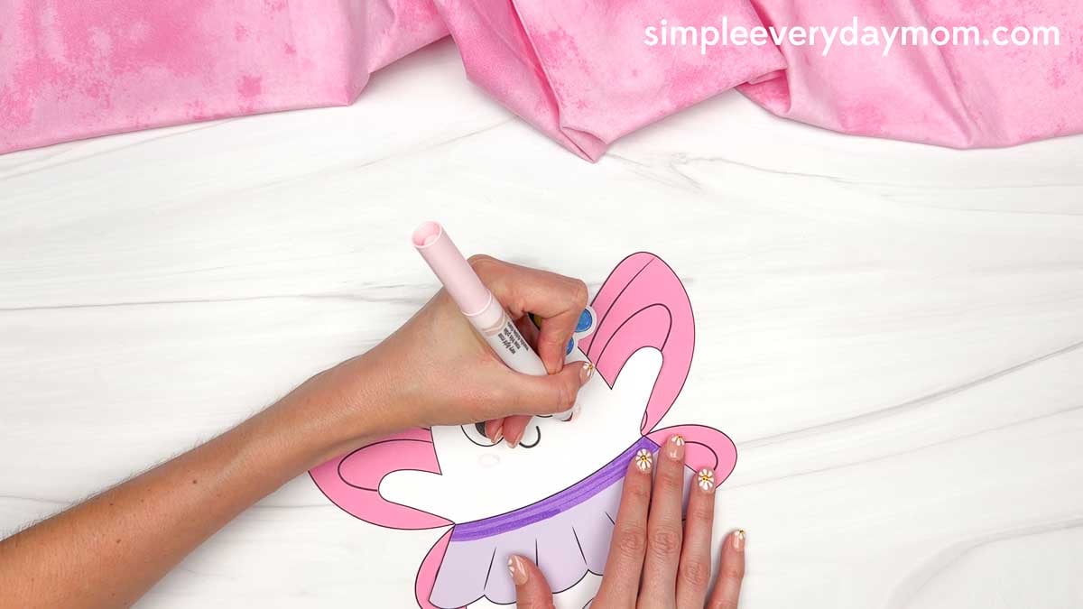 Hands adding pink blush to the Fairy Ghost Disguise Craft face with a marker.