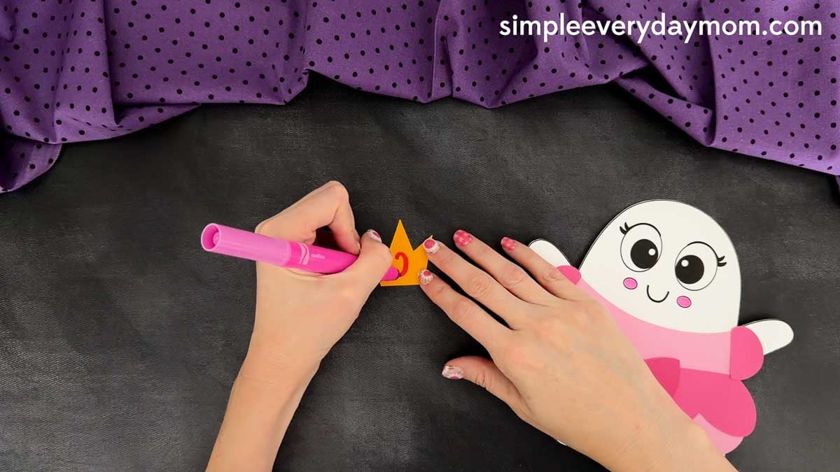 Hands coloring the jewel on the Princess Ghost Disguise Craft crown before attaching it above the ghost's head.