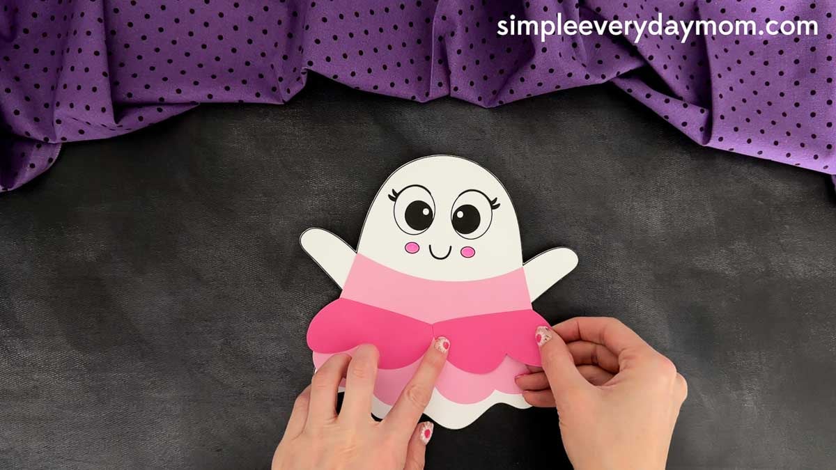 Hands positioning the top layer of the princess dress onto the ghost body, lining it up above the bottom dress layer.