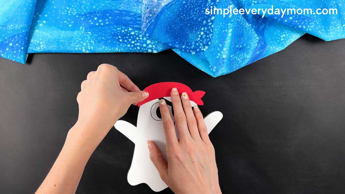 Hands gluing the pirate bandana across the top of the ghost's head above the eye.