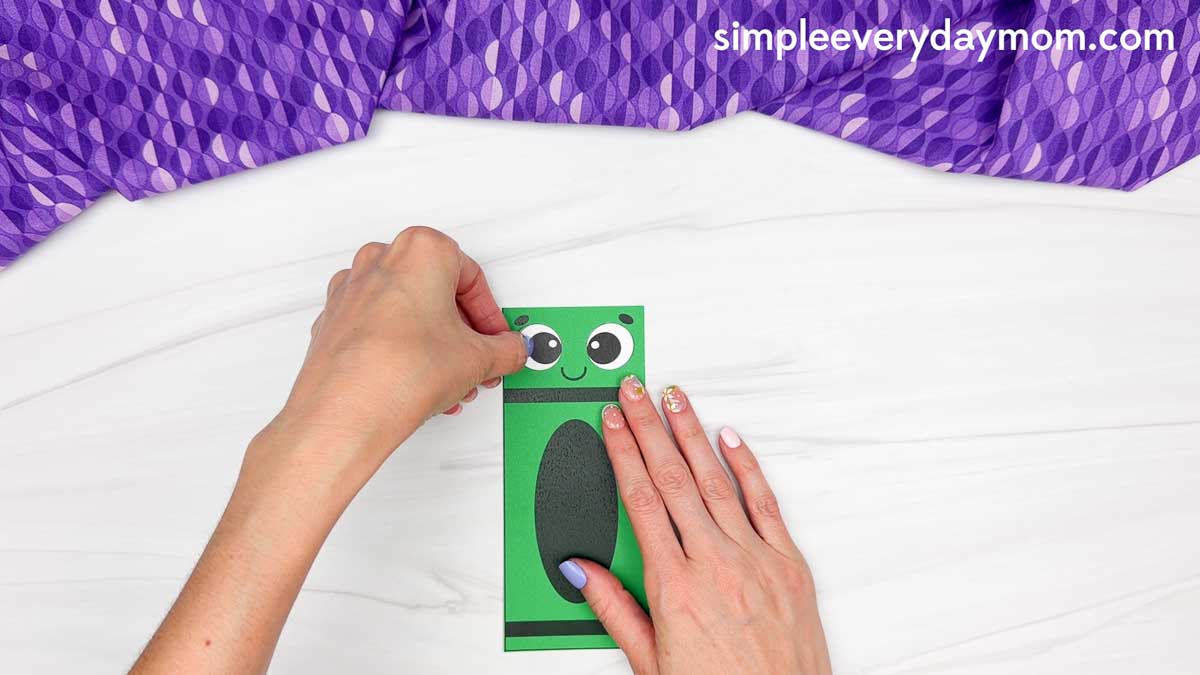 Hands pressing the eye onto the crayon shape craft while holding the body steady.