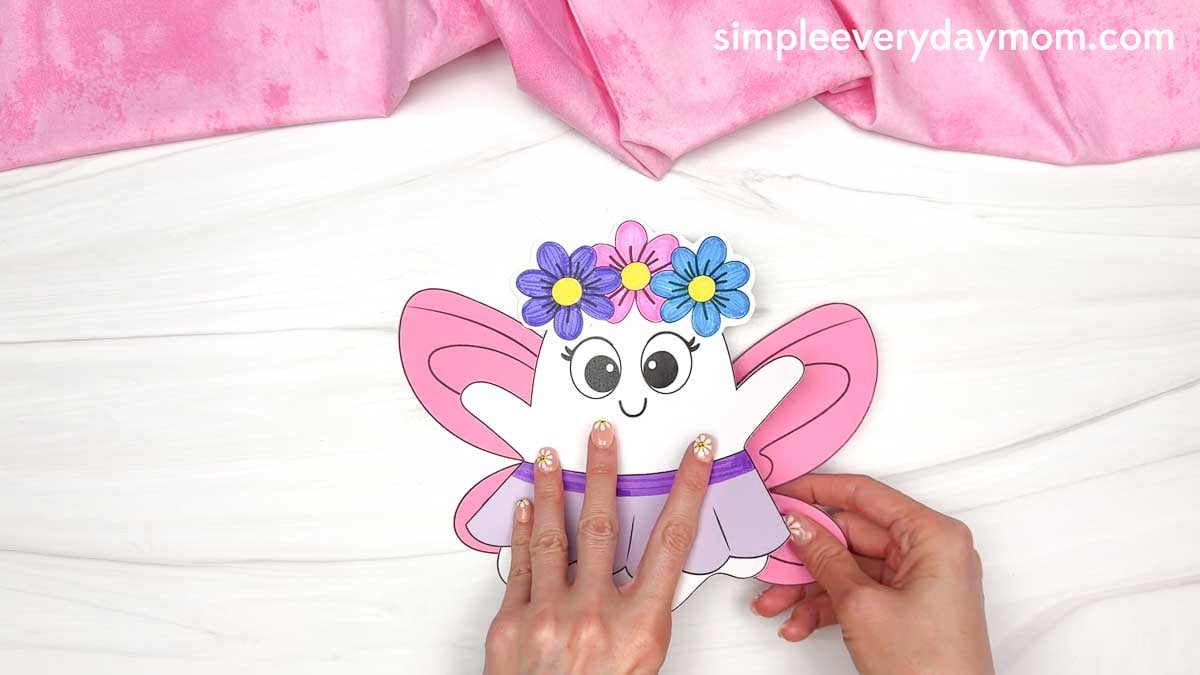 Hands attaching the fairy wings behind the Fairy Ghost Disguise Craft body to complete the costume.