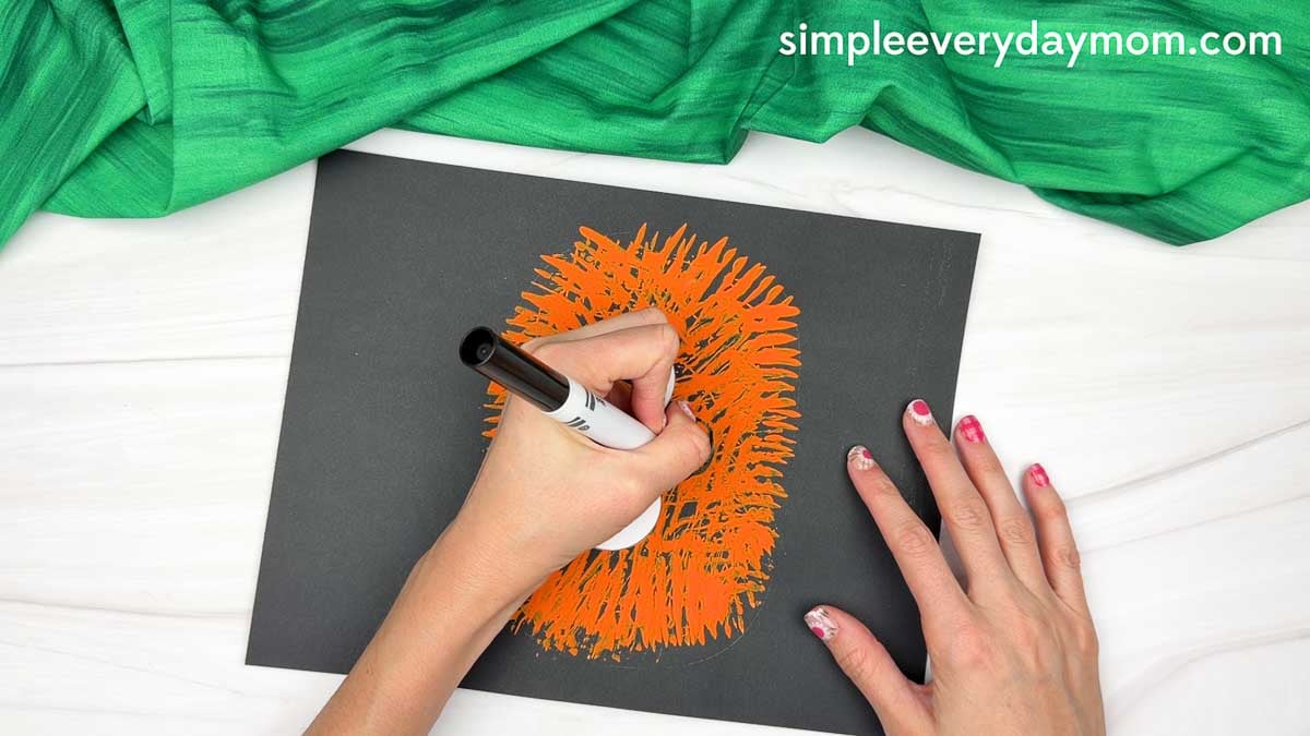 Hands drawing the pumpkin smile below the eyes with a black marker.