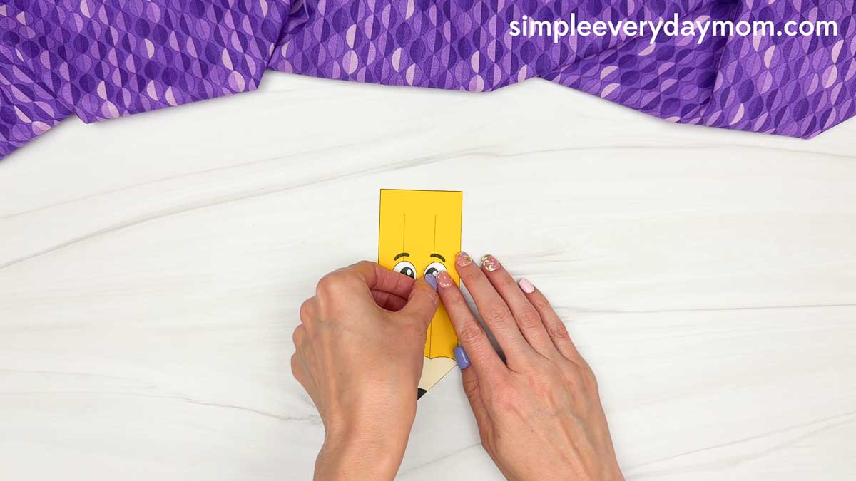 Hands attach the eyes to the smiling pencil craft face.