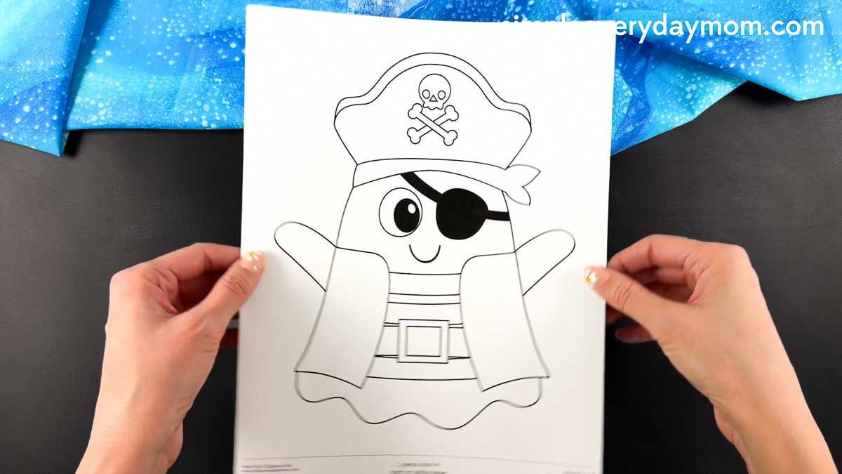 Hands holding the pirate ghost template with the pirate hat, eye patch, and sleeve pieces before assembly.