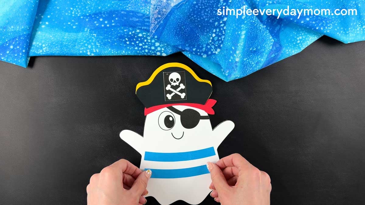 Hands positioning the two shirt stripes across the middle of the ghost's body before gluing them in place.