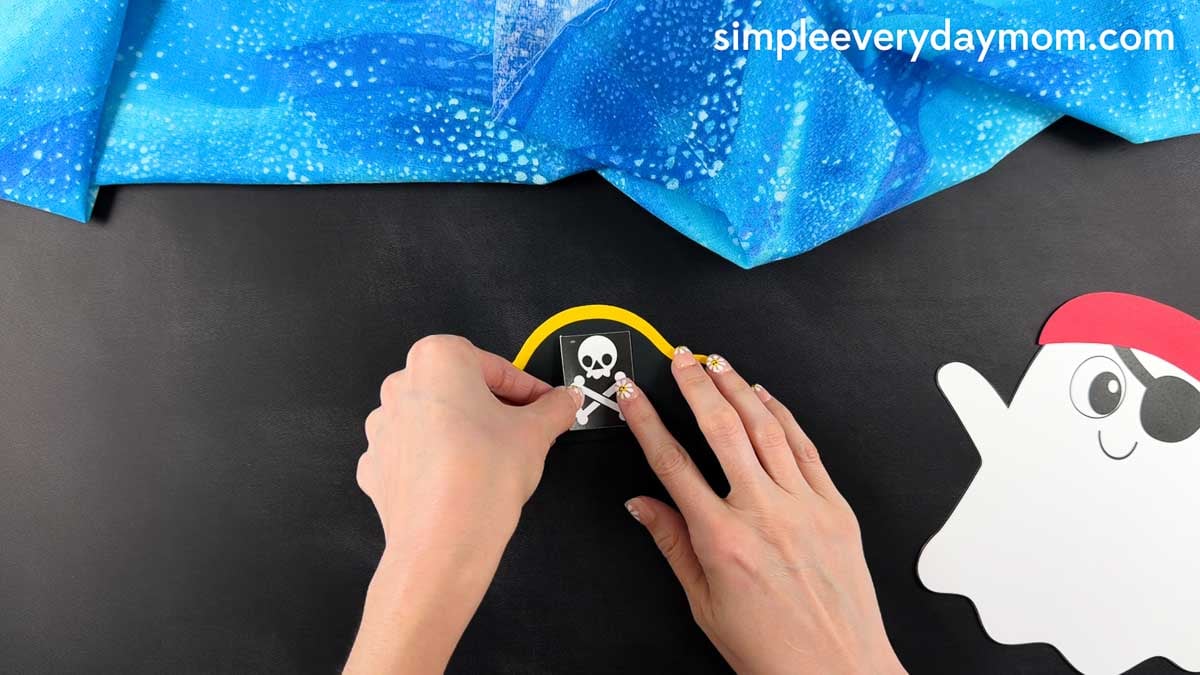 Hands gluing the skull and crossbones emblem to the center of the pirate hat.