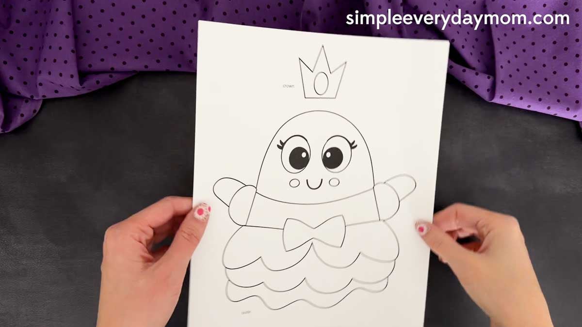 Hands holding the Princess Ghost Disguise Craft template with the ghost body, arms, bow, layered dress, and crown pieces ready to cut out.