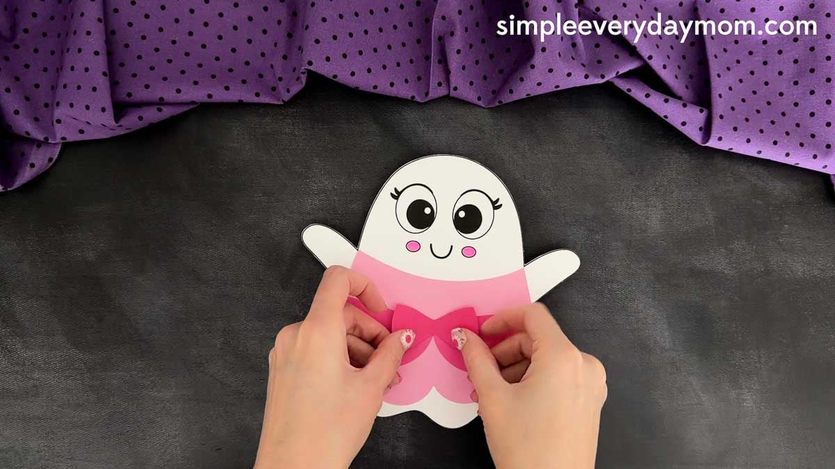Hands placing the bow at the center of the princess dress on the Princess Ghost Disguise Craft.