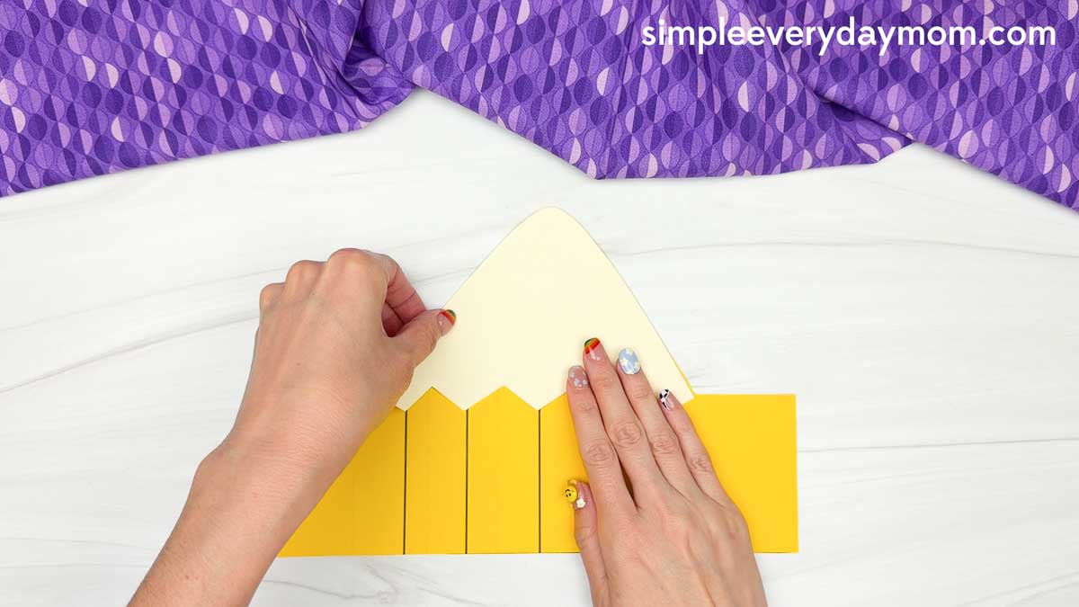Hands glue the pencil wrapper piece onto the printable pencil headband template.
