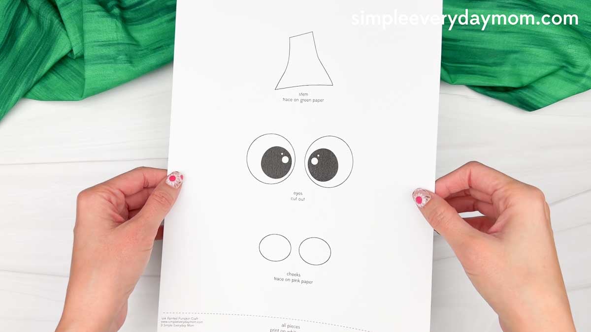 Hands holding the Fork Painted Pumpkin Craft template showing the face outline, eyes, and cheek pieces before cutting.