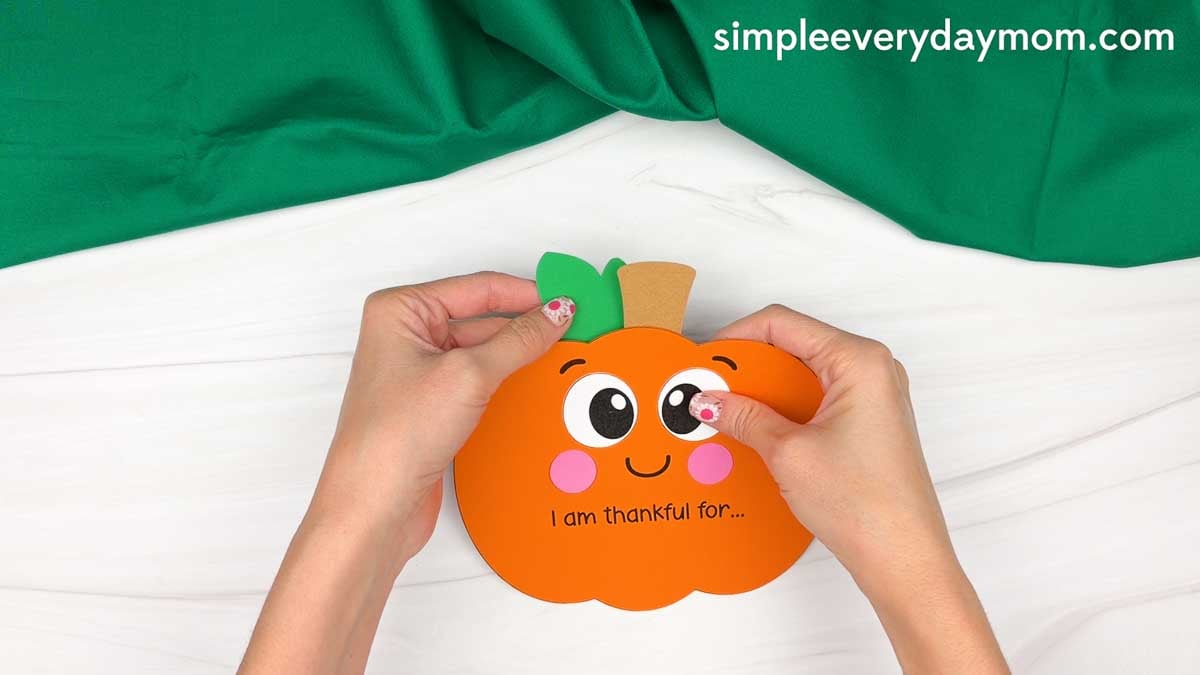 Hands gluing the leaf to the top of the thankful pumpkin beside the stem.